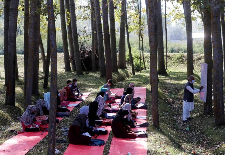Students wearing protective face masks attend their class under the trees as they maintain social distancing outside their school in Gund on the outskirts of Srinagar. REUTERS/Danish Ismail  